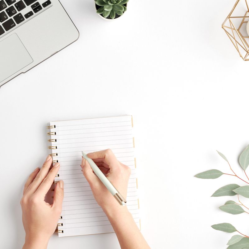 Hands of young female office worker holding pen over blank page of notebook while planning work by desk